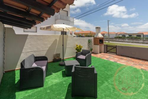 a patio with green grass and chairs and an umbrella at Baleal Classic Waves Guest House in Baleal