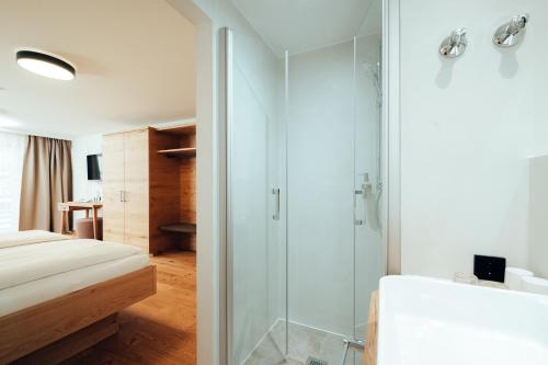 a bathroom with a glass shower and a bed at Hotel Tradizio in Mittelberg