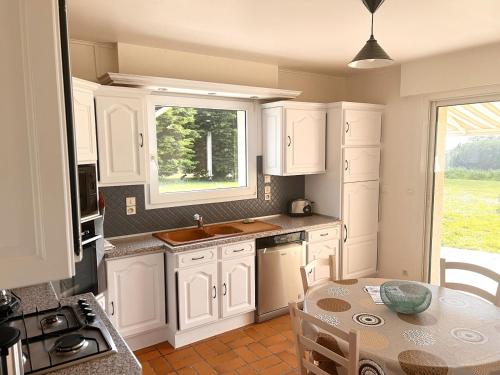 une cuisine avec des armoires blanches, une table et une fenêtre dans l'établissement La Maison de L'Hermitage 225 m2 terrain 2300 m2, à Planguenoual