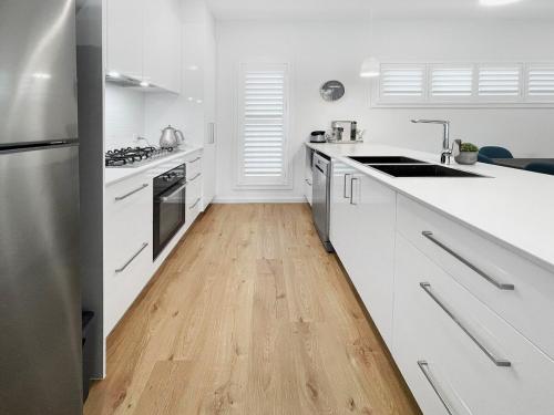 a kitchen with white cabinets and a wooden floor at Coastline Cove - Modern Townhome Oasis in Shellharbour