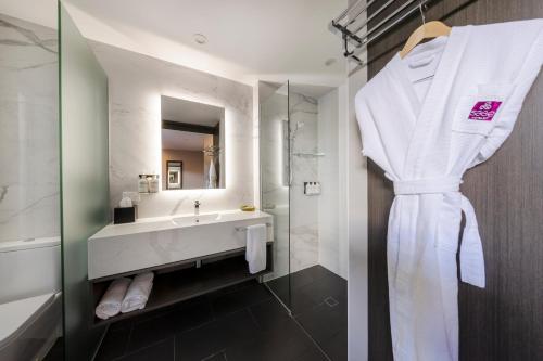 a bathroom with a white robe hanging on a wall at Sage Hotel James Street in Brisbane
