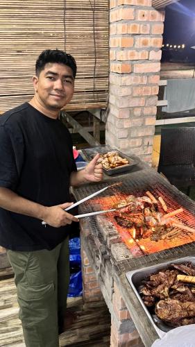 a man standing next to a grill with meat at Rajawali Riverside Retreat in Dungun
