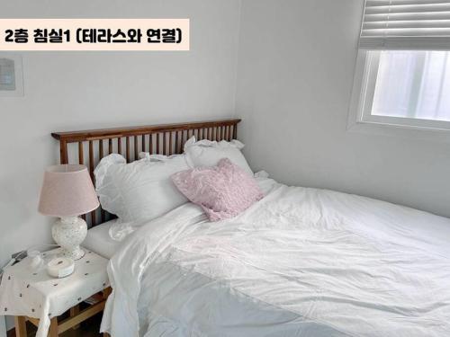 a white bed with a pink pillow on top of it at Juns House 대인원 수용 가능, 2층 복층 주택, 테라스보유, 가족숙소 적합 in Pohang