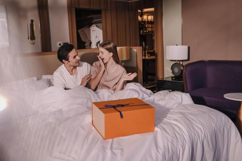 a man and woman sitting on a bed with a box at Nysa Hotel Bangkok Sukhumvit 11 in Bangkok