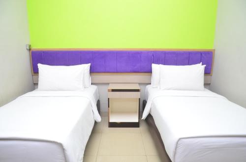 two twin beds in a room with green and purple at Alodia Powered by Archipelago in Tanjungkarang