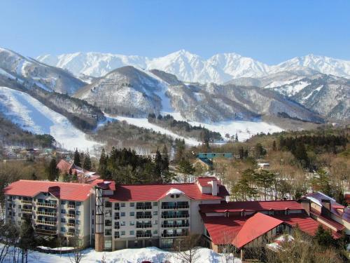 a building with a red roof in front of a mountain at Hakuba Tokyu Hotel in Hakuba