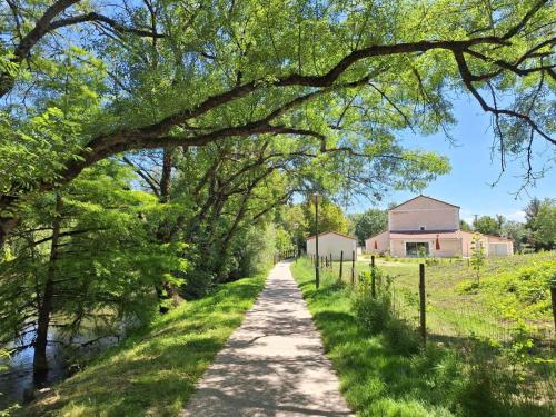 une route bordée d'arbres avec une ferme au loin dans l'établissement Au son de l'eau, à Birac