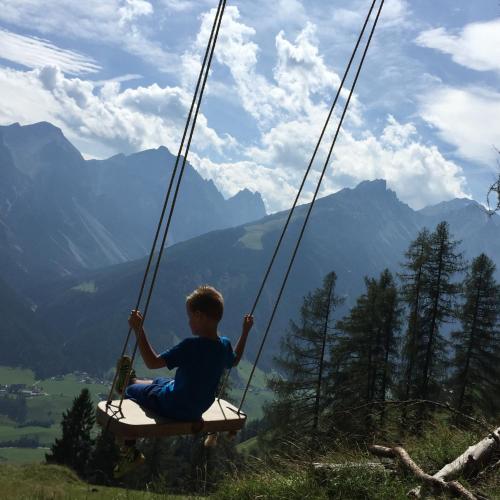 a boy sitting on a swing in the mountains at Alpenhotel Tirolerhof in Neustift im Stubaital