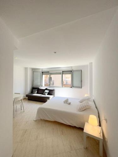 a white bedroom with a bed and a living room at M2 Apartament cèntric in Terrassa