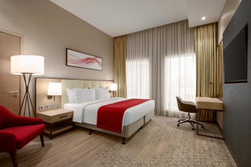 a hotel room with a bed and a red chair at Ramada by Wyndham Riyadh King Fahd Road in Riyadh