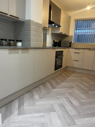 a kitchen with white cabinets and a wooden floor at Ilayda Stays - 22 Alexandra Street in Port Talbot