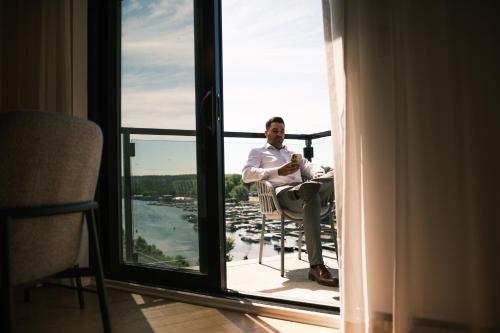 a man sitting in a chair looking out a window at Hôtel Expérience - Quartier Des Marinas in Magog-Orford