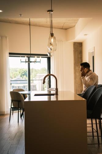 a man sitting in a kitchen talking on a cell phone at Hôtel Expérience - Quartier Des Marinas in Magog-Orford