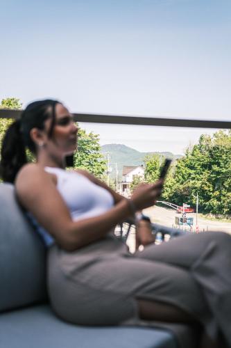 a pregnant woman sitting on a couch looking at her cell phone at Hôtel Expérience - Quartier Des Marinas in Magog-Orford