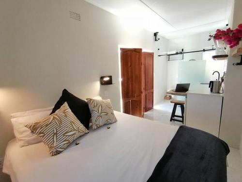 a bedroom with a white bed with pillows and a kitchen at Melkbos Sea Spray Studio Apartment in Cape Town