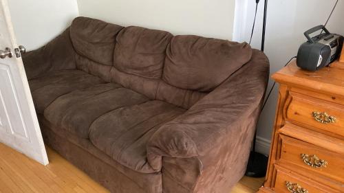 a brown couch in the corner of a room at Private Rooms, Free Parking, Full Kitchen, Best Prices in Town- York University Heights in Toronto