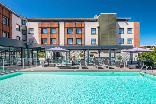 a swimming pool with chairs and umbrellas in front of a building at Holiday Inn Toulouse Airport by IHG in Blagnac