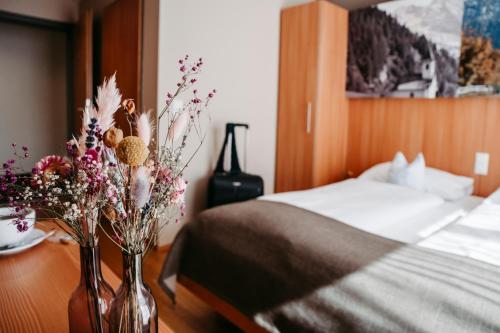 two vases with flowers on a table next to a bed at JUFA Hotel Wipptal in Steinach am Brenner