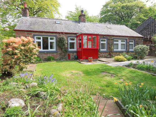 a small house with a red door in a garden at The Cottage in Kirriemuir