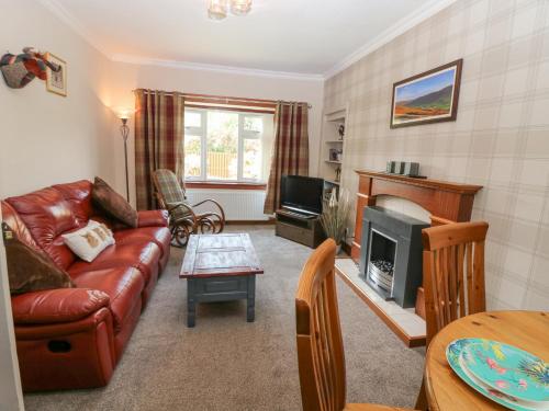 a living room with a leather couch and a fireplace at The Cottage in Kirriemuir