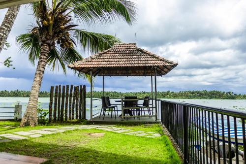 a table and chairs under a gazebo next to the water at Jai Lake House in Perumbalam