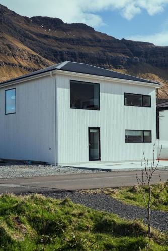 a white building with a mountain in the background at Nyrenoveret, moderne,hyggeligt hus in Leirvík