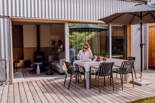 a woman sitting at a table on a patio at Domki Płyniewoda - całoroczne domy PREMIUM, klimatyzacja, kominek, blisko morza in Dziwnów