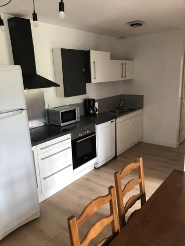 une cuisine avec des armoires blanches et une table et des chaises dans l'établissement Appartement St Cyr Coëtquidan, à Guer