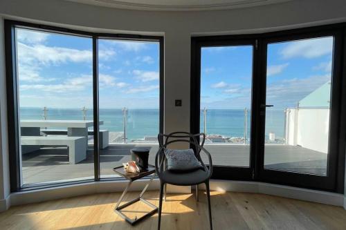 a chair and a table in a room with windows at Seasalt - Beach Front Apartment in Woolacombe