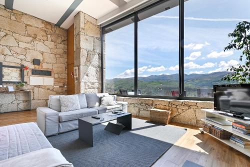 a living room with a couch and a tv and large windows at Casas das Olas in Arcos de Valdevez