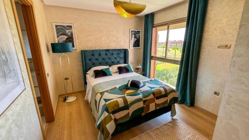 Un dormitorio con una cama con cabecero azul y una ventana. en Dar Emna - Appartement de prestige sur golf, en Marrakech