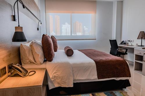 a bedroom with a bed with a desk and a window at Hotel Barranquilla Plaza in Barranquilla