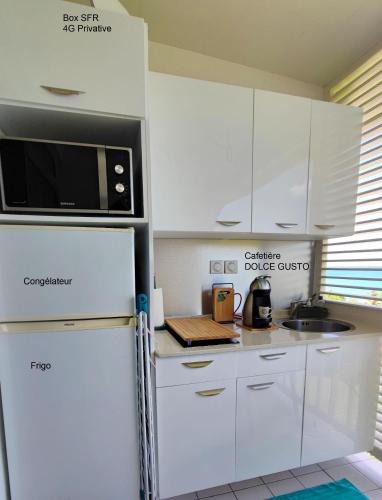 a white kitchen with a microwave and a refrigerator at Un petit joyau in Le Diamant