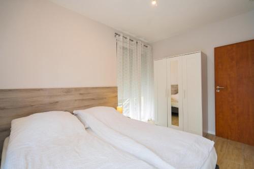 a bedroom with a white bed and a wooden cabinet at Riviéra Apartmanház in Siófok
