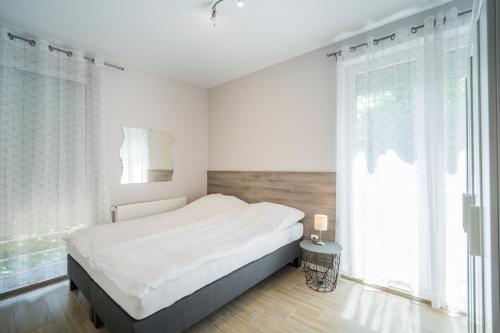 a white bedroom with a bed and a large window at Riviéra Apartmanház in Siófok