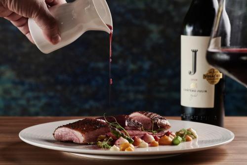 a person pouring wine into a plate of meat at Amira Luxury Resort & Spa - Adults Only in Adelianos Kampos