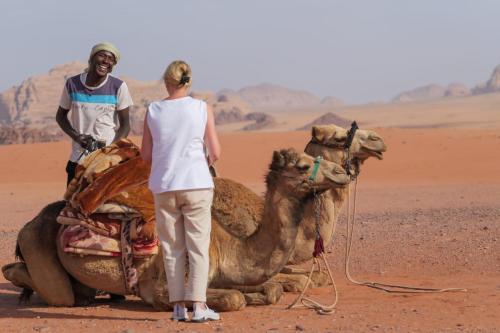 a man and a woman standing next to a camel in the desert at Wadi Rum Desert Adventures in Wadi Rum