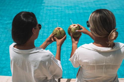 two women sitting next to a swimming pool holding fruit at Quality - Boas Vistas in Canoa Quebrada