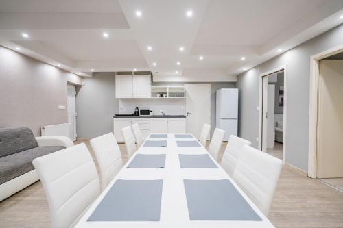 a white dining room with a long table and white chairs at Riviéra Apartmanház in Siófok