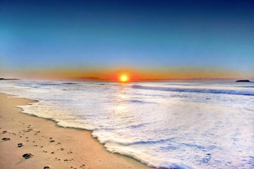 a beach with the sun rising over the ocean at Sapphire Beach Holiday Park in Coffs Harbour