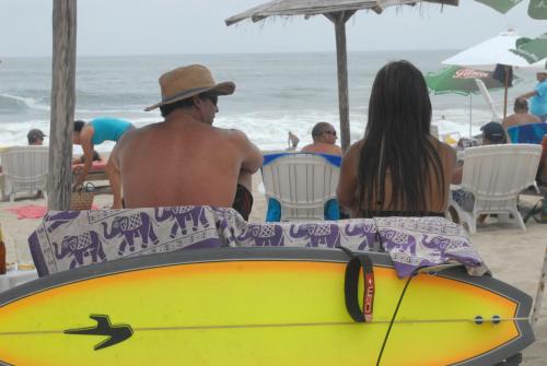 a man and a woman sitting on the beach with a surfboard at Hamacas in Punta Negra