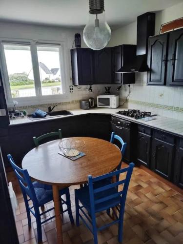 une cuisine avec une table en bois et des chaises bleues dans l'établissement Maison de Vacances à Guissény - Idéal pour Familles et Amis, à Guissény
