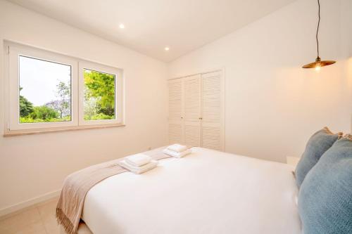 a white bedroom with a bed and a window at GuestReady - Casa do Jacarandá in Paço de Arcos