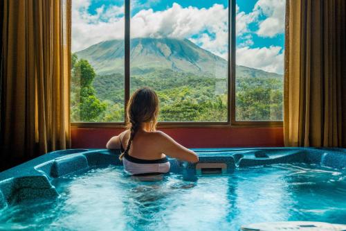a woman sitting in a hot tub looking out a window at Hotel Arenal Kioro Suites & Spa in Fortuna