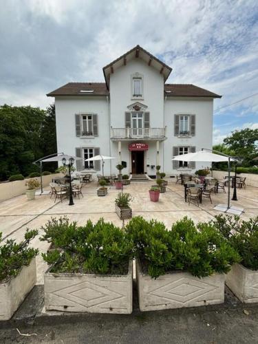 a large white building with a patio with tables and chairs at Logis Hôtel & Restaurant Le Parcey in Parcey