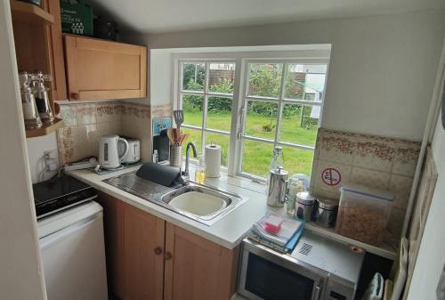 a small kitchen with a sink and a window at The Old Dairy, comfy 1 bedroom apartment with lounge,bathroom and kitchenette near town, pubs and walks in Ringwood