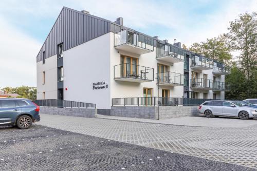 a white building with cars parked in a parking lot at Kamienica Parkowa in Dąbki