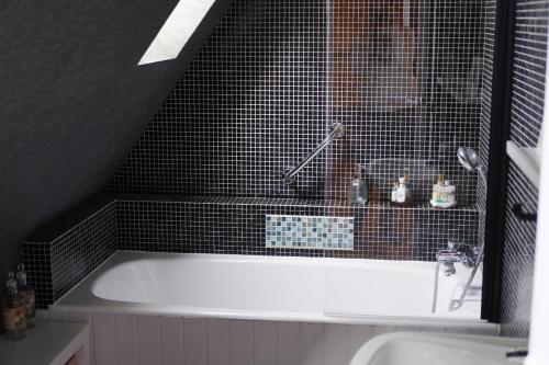 a bath tub in a bathroom with black tiles at La Chambre d'Agapè in Fouesnant
