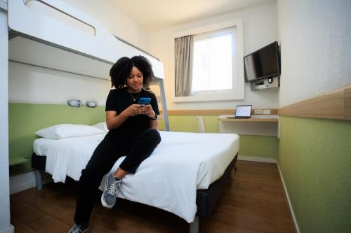 a woman sitting on a bed looking at her cell phone at ibis budget Belo Horizonte Minascentro in Belo Horizonte