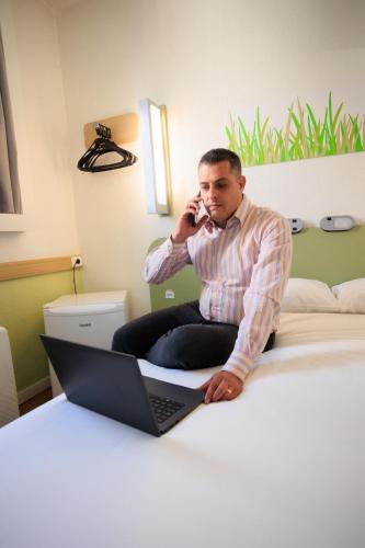 a man sitting on a bed talking on a cell phone at ibis budget Belo Horizonte Minascentro in Belo Horizonte